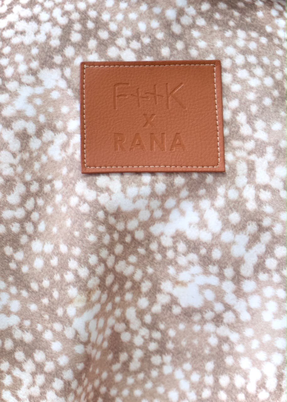 Close-up of the tan embossed F++K x RANA patch on the taupe-and-white spotted Bambi White Boy Jacket