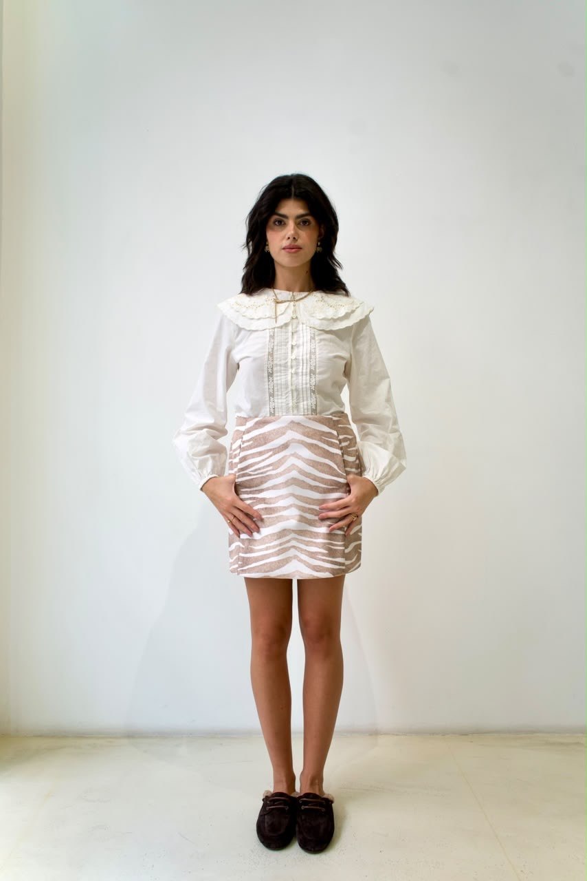 Full-length front styling view of the taupe-and-white zebra mini skirt with a white blouse