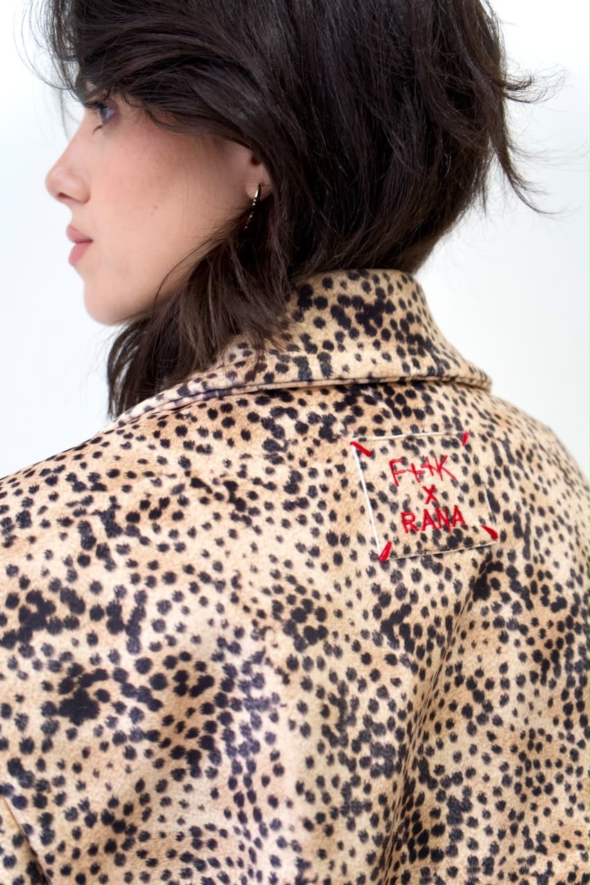 Back shoulder detail of the cheetah-print bomber jacket, showing the raised collar and red embroidered F++K x RANA patch