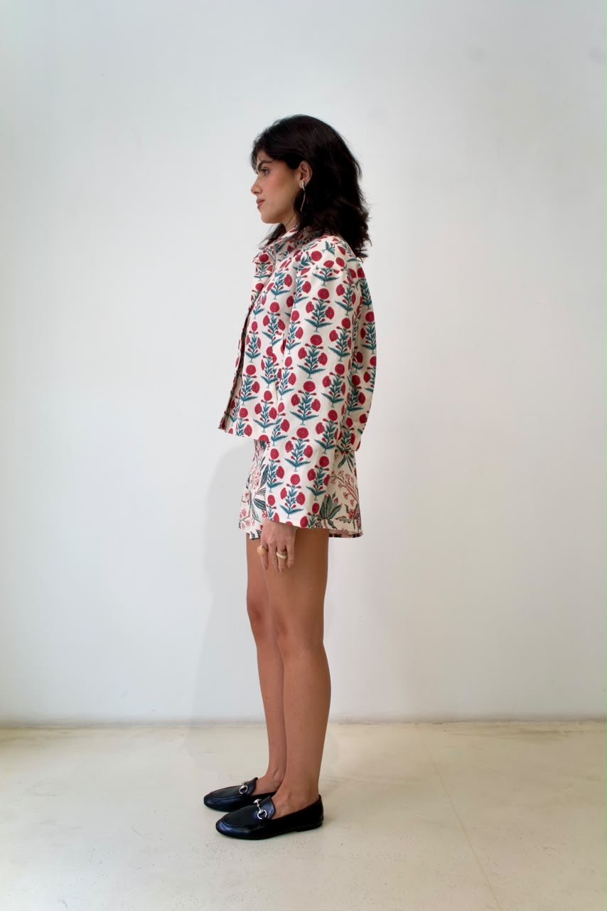 Full-length side styling view of the Indian Flower bomber jacket with repeating red botanical motifs and teal-green leaves, worn with contrasting floral shorts